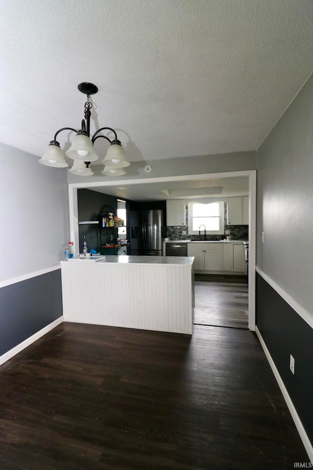 kitchen featuring white cabinetry, appliances with stainless steel finishes, decorative light fixtures, a textured ceiling, and dark hardwood / wood-style flooring