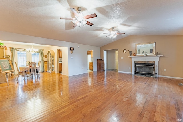 unfurnished living room with a tiled fireplace, ceiling fan with notable chandelier, light hardwood / wood-style flooring, and vaulted ceiling