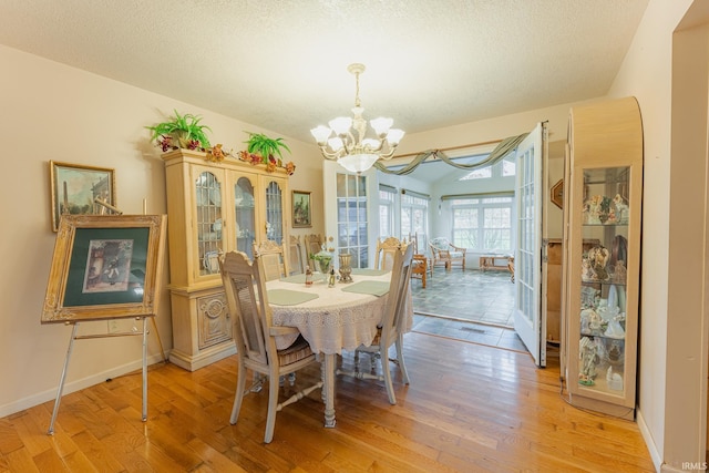 dining area with light hardwood / wood-style floors, a textured ceiling, and an inviting chandelier