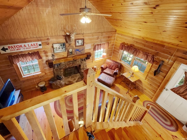 living room with wood walls, wooden ceiling, ceiling fan, wood-type flooring, and a stone fireplace