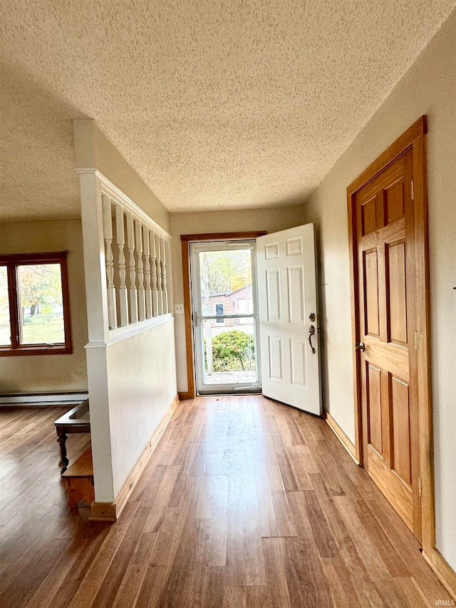 doorway featuring baseboard heating, wood-type flooring, and a textured ceiling