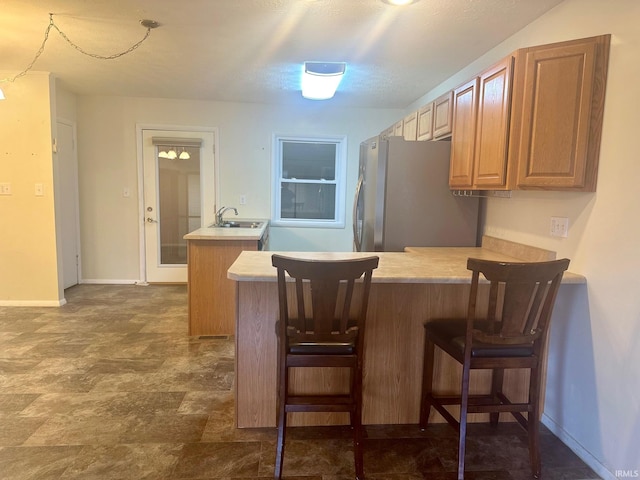 kitchen featuring a kitchen bar, kitchen peninsula, a textured ceiling, sink, and stainless steel refrigerator