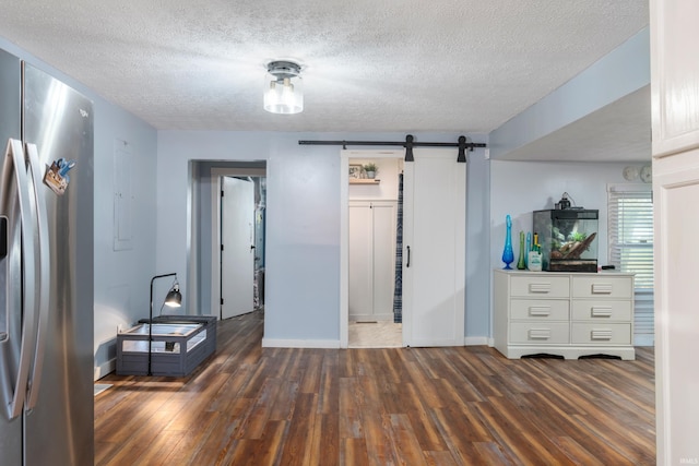 interior space featuring a textured ceiling, a spacious closet, a barn door, stainless steel fridge, and dark hardwood / wood-style flooring