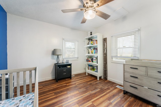 bedroom featuring dark hardwood / wood-style flooring, a nursery area, a textured ceiling, and ceiling fan