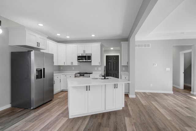 kitchen with light wood-type flooring, appliances with stainless steel finishes, a kitchen island with sink, and white cabinets