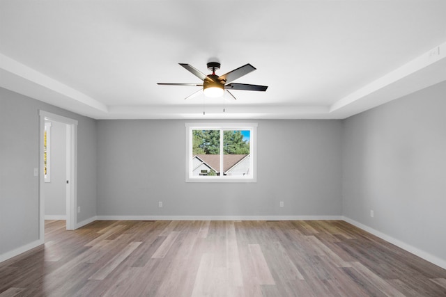 empty room featuring light wood-type flooring, ceiling fan, and a tray ceiling