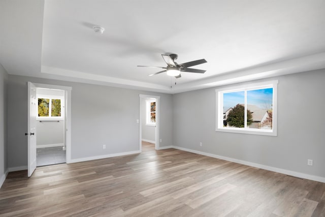 spare room with ceiling fan, a healthy amount of sunlight, a raised ceiling, and light wood-type flooring