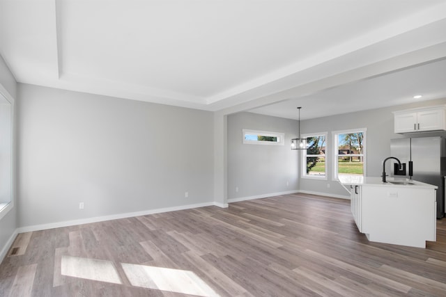 interior space featuring light wood-type flooring, a chandelier, sink, and a raised ceiling