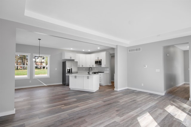 kitchen with stainless steel appliances, hardwood / wood-style flooring, decorative light fixtures, a kitchen island with sink, and white cabinets