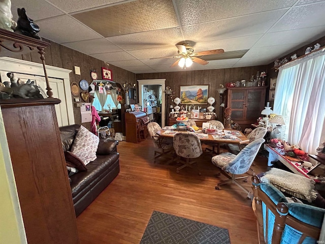 interior space with a drop ceiling, hardwood / wood-style floors, wooden walls, and ceiling fan