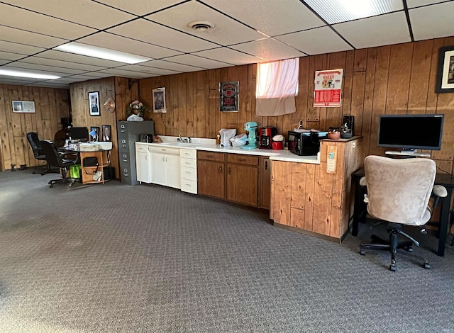 office space with dark colored carpet, a paneled ceiling, and wood walls