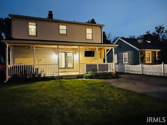 back house at dusk with a yard and covered porch