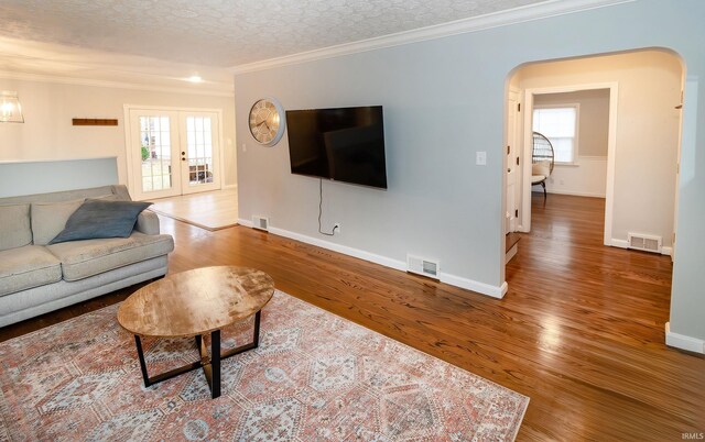 living room featuring wood-type flooring, a textured ceiling, french doors, and crown molding