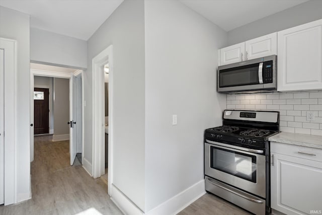 kitchen with backsplash, appliances with stainless steel finishes, light hardwood / wood-style floors, and white cabinets