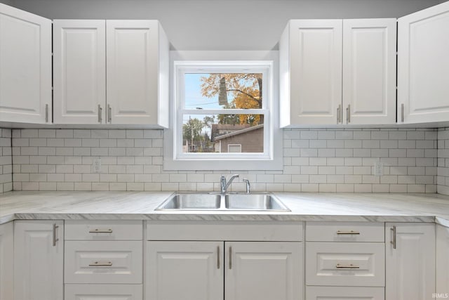 kitchen with white cabinetry, decorative backsplash, sink, and light stone counters