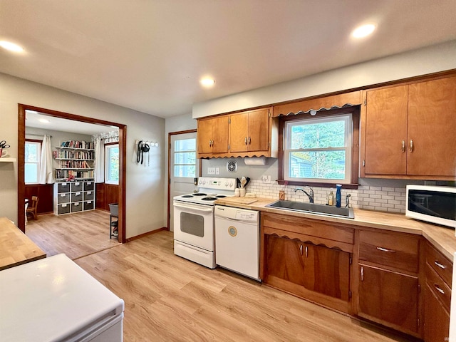 kitchen featuring light wood-type flooring, white appliances, sink, and backsplash