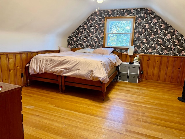 bedroom featuring wooden walls, light wood-type flooring, and vaulted ceiling