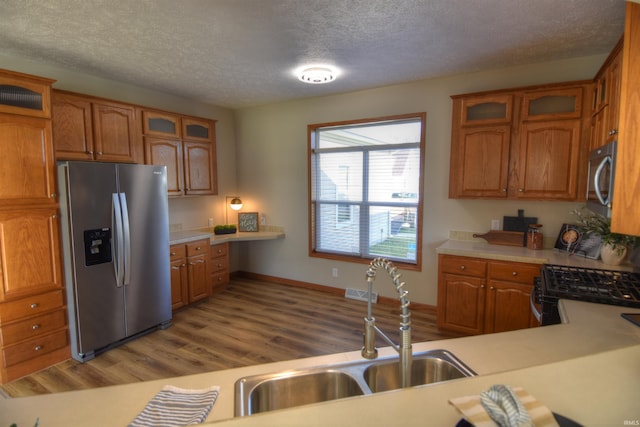 kitchen with stainless steel appliances, a textured ceiling, sink, and light hardwood / wood-style flooring