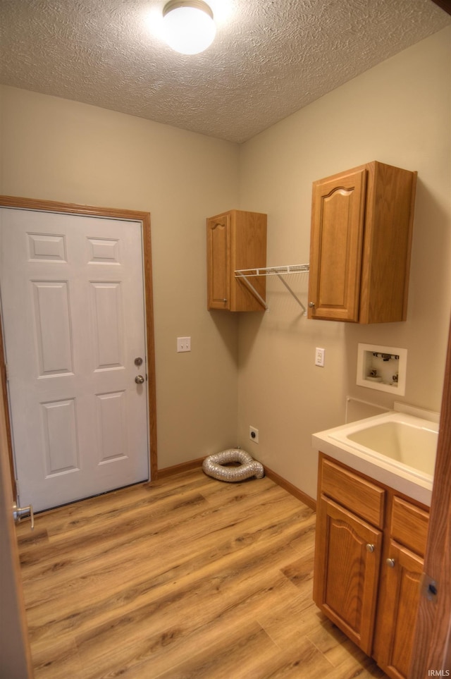 clothes washing area with electric dryer hookup, cabinets, a textured ceiling, light hardwood / wood-style flooring, and hookup for a washing machine