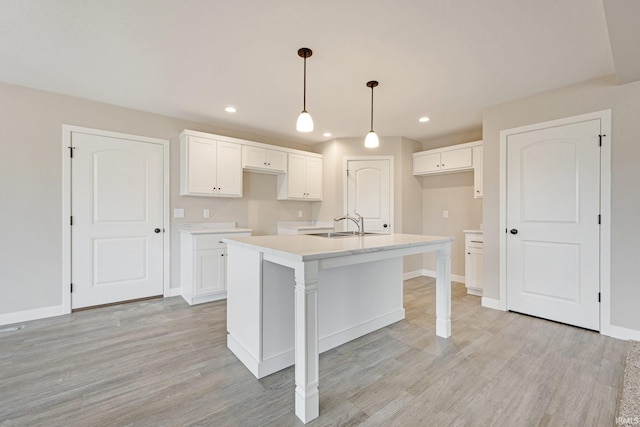 4805 Falcon Pkwy, New Haven, IN 46774 - kitchen with light wood-type flooring, white cabinets, a kitchen island with sink, a sink, and baseboards