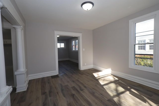 unfurnished room with ornate columns, dark wood-type flooring, and a healthy amount of sunlight