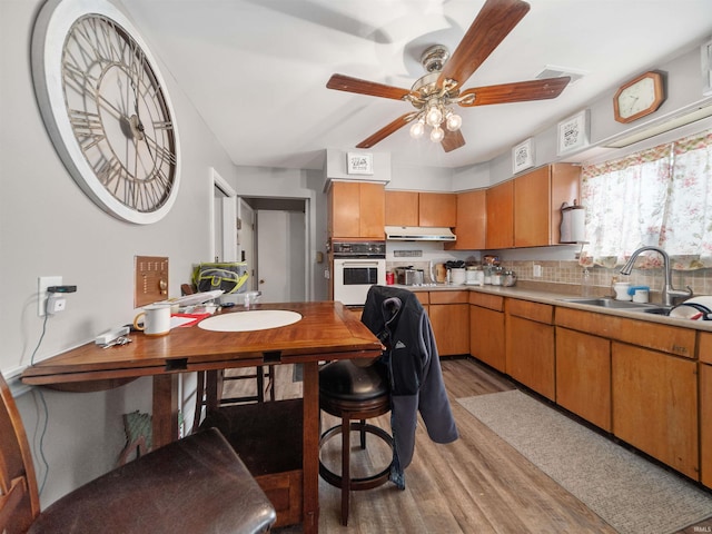 kitchen with ceiling fan, white oven, sink, and light hardwood / wood-style flooring