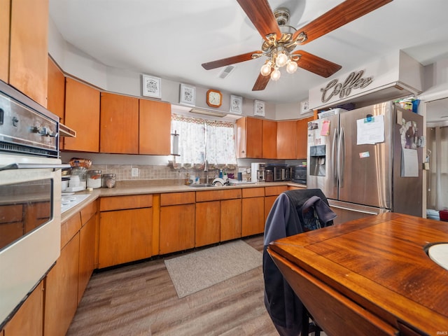 kitchen with stainless steel appliances, tasteful backsplash, light hardwood / wood-style floors, sink, and ceiling fan