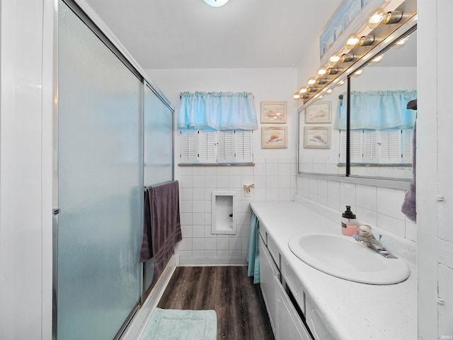 bathroom featuring tasteful backsplash, tile walls, wood-type flooring, an enclosed shower, and vanity