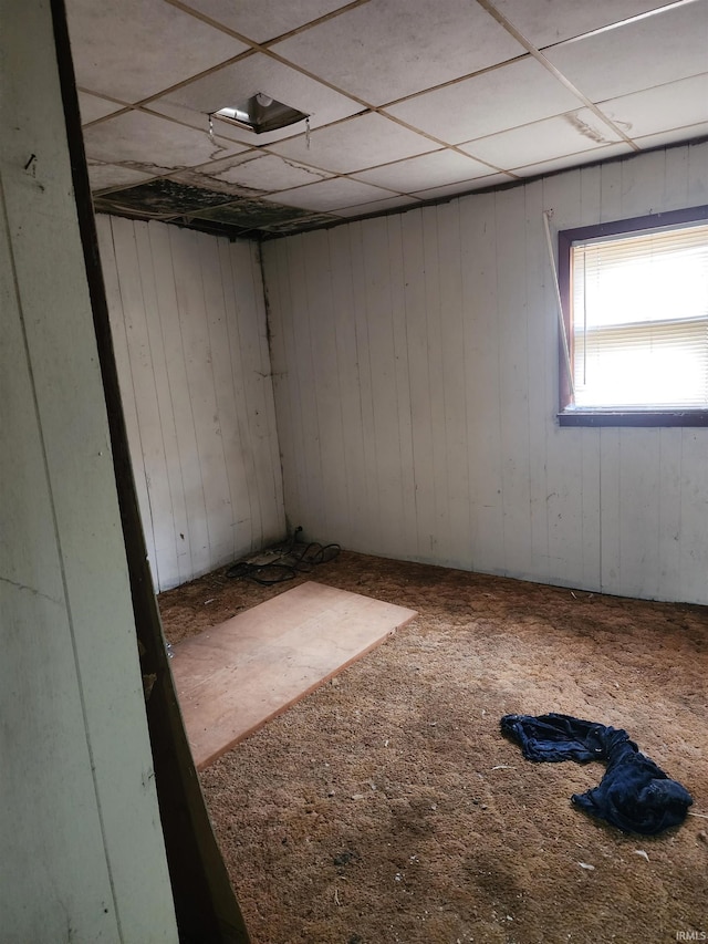 basement with carpet, a paneled ceiling, and wooden walls