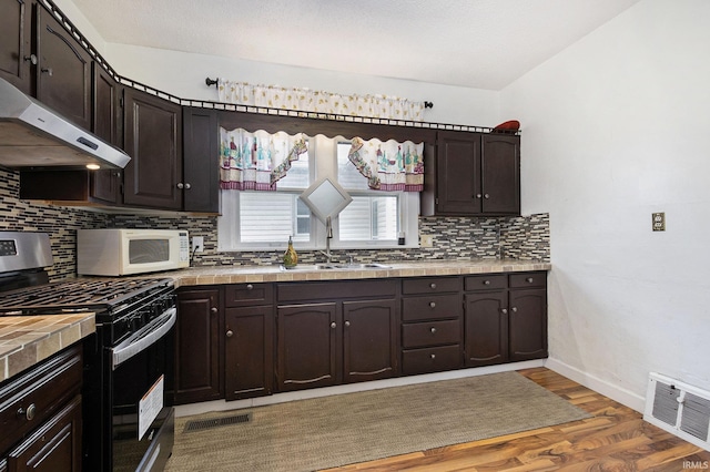 kitchen with gas range, sink, dark hardwood / wood-style floors, backsplash, and dark brown cabinets