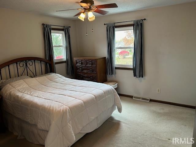 carpeted bedroom featuring a textured ceiling, multiple windows, and ceiling fan