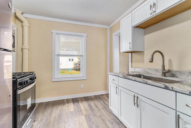 kitchen with black gas range oven, light stone countertops, sink, light hardwood / wood-style floors, and white cabinets