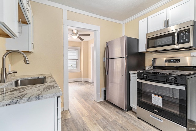 kitchen featuring stainless steel appliances, sink, light stone countertops, white cabinets, and light wood-type flooring