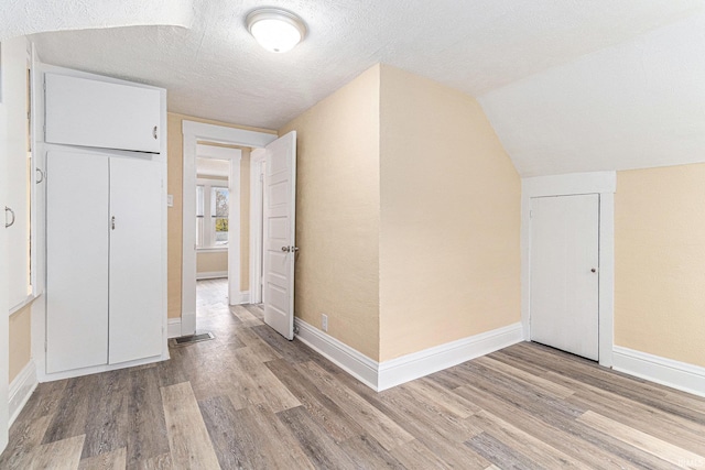 bonus room with light wood-type flooring, lofted ceiling, and a textured ceiling