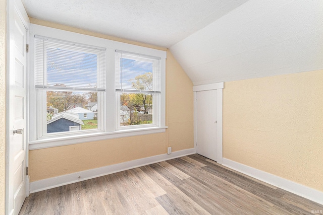 additional living space featuring light wood-type flooring, vaulted ceiling, and a textured ceiling