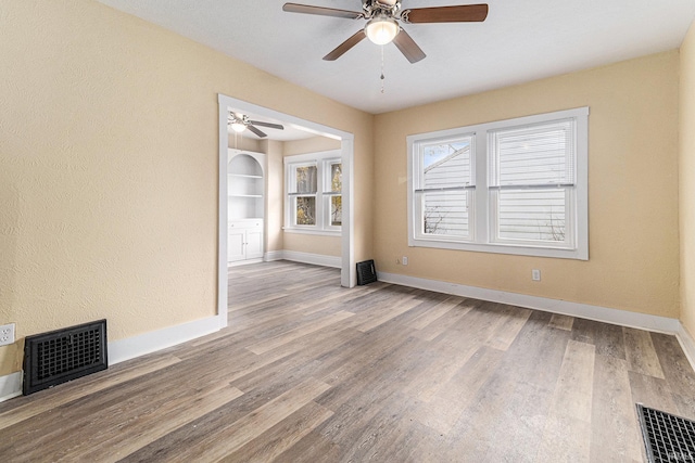 unfurnished room featuring built in shelves, hardwood / wood-style flooring, and ceiling fan