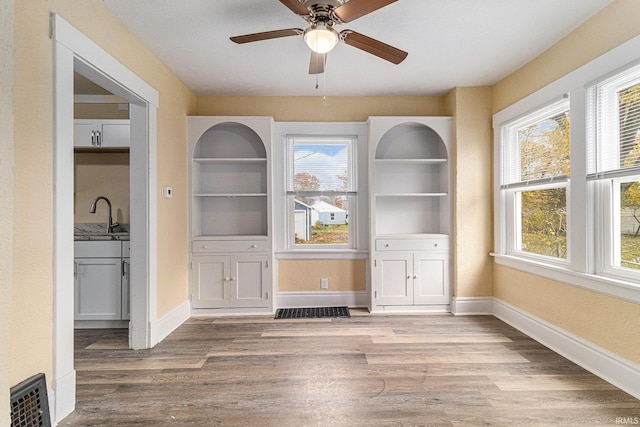 unfurnished dining area with sink, ceiling fan, wood-type flooring, and a healthy amount of sunlight