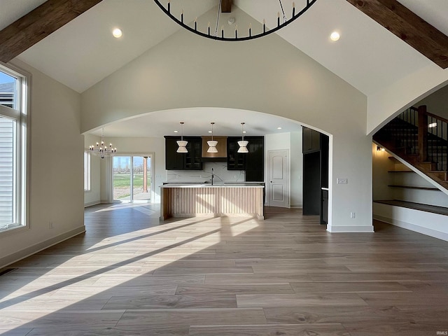 unfurnished living room featuring high vaulted ceiling, beamed ceiling, a chandelier, and light wood-type flooring