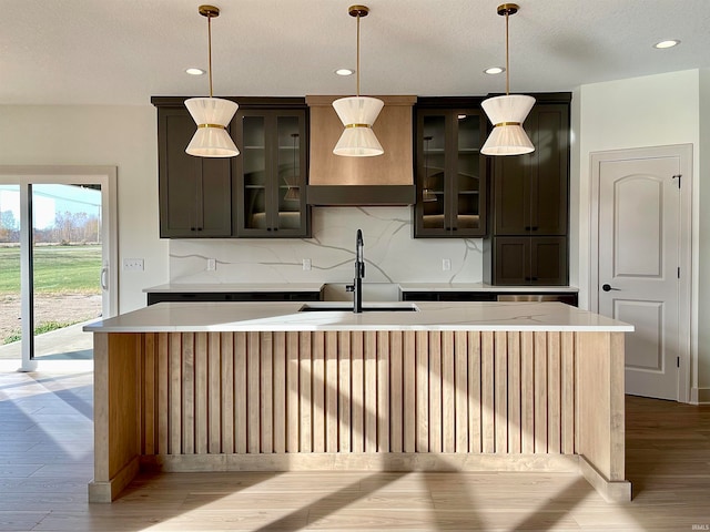 kitchen with dark brown cabinets, light wood-type flooring, decorative light fixtures, and an island with sink