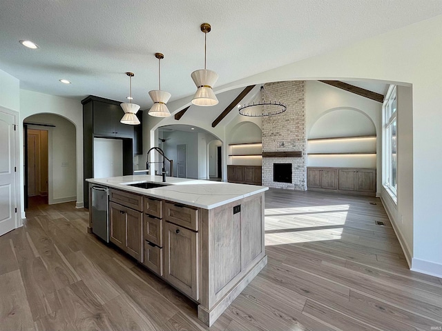 kitchen with a center island with sink, decorative light fixtures, light stone countertops, sink, and stainless steel dishwasher