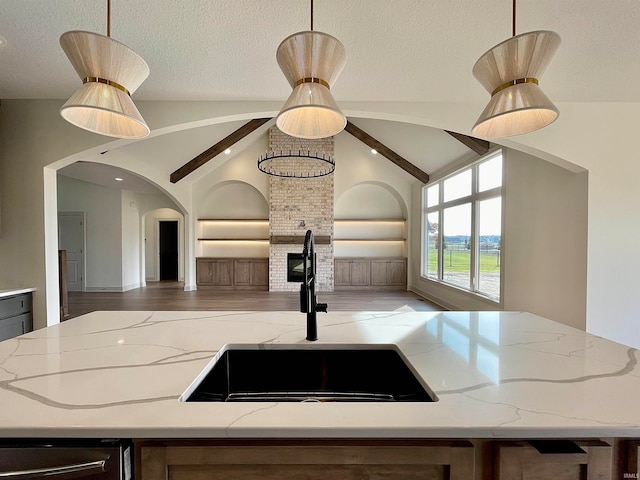 kitchen with lofted ceiling with beams, pendant lighting, sink, and light stone counters