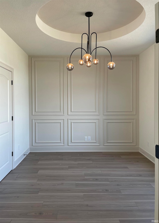 unfurnished dining area featuring a textured ceiling, dark hardwood / wood-style flooring, and a tray ceiling