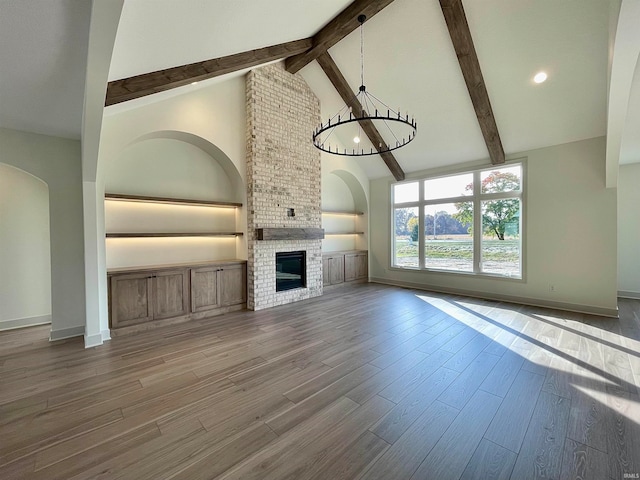 unfurnished living room with hardwood / wood-style floors, a fireplace, beam ceiling, and a notable chandelier