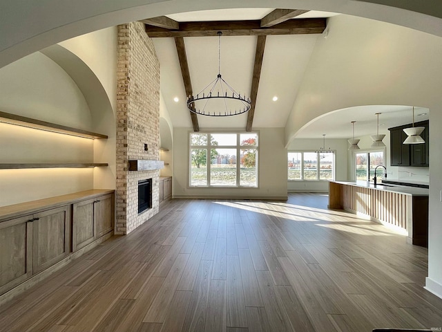 unfurnished living room with an inviting chandelier, hardwood / wood-style floors, high vaulted ceiling, beamed ceiling, and a fireplace