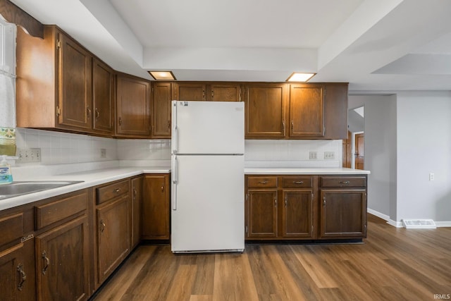 kitchen featuring dark wood-type flooring, sink, backsplash, and white refrigerator