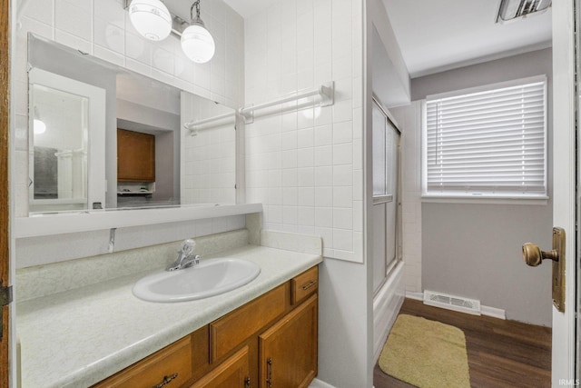 bathroom with bath / shower combo with glass door, wood-type flooring, and vanity