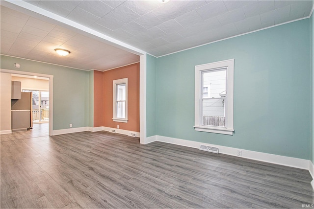 empty room featuring wood-type flooring, plenty of natural light, and crown molding