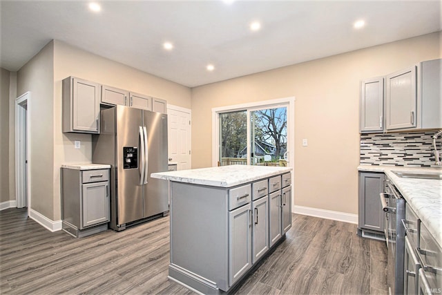 kitchen featuring stainless steel appliances, gray cabinets, dark hardwood / wood-style flooring, decorative backsplash, and a center island