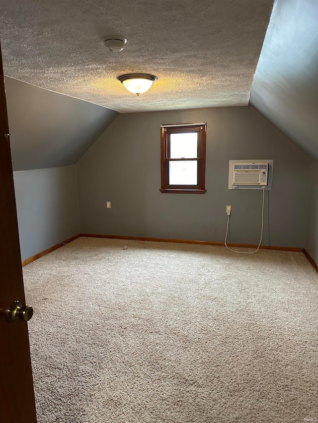 bonus room with a wall unit AC, a textured ceiling, vaulted ceiling, and carpet