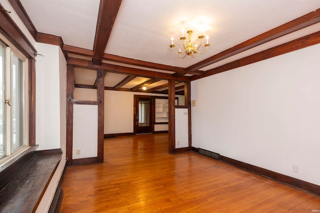 empty room with beamed ceiling, wood-type flooring, a healthy amount of sunlight, and a notable chandelier